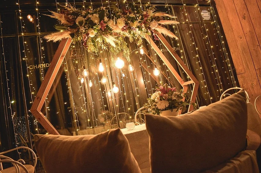 Ambientación real de Madero: arco de madera, flores, lámparas y sillones bajo guirnaldas